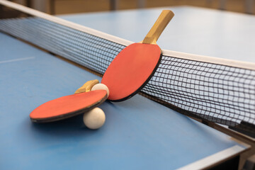 Table tennis ping pong paddles and white ball on blue board.