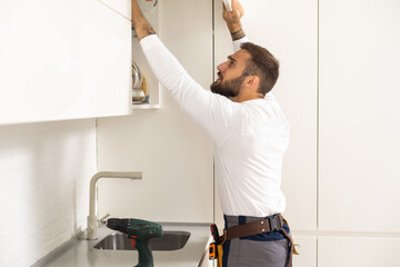 Two handymen, workers in uniform fixing, installing furniture and equipment in the kitchen, using screwdriver indoors. Furniture repair and assembly concept.