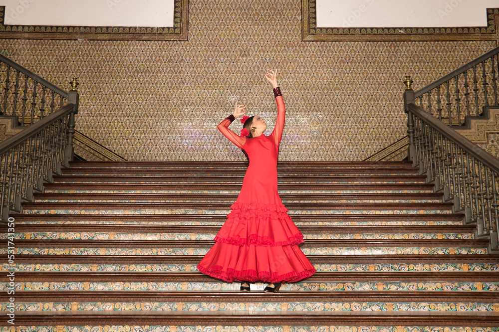 Canvas Prints Young teenage woman in red dance suit with ruffles and red carnations in her hair dancing flamenco on stairs. Flamenco concept, dance, art, typical Spanish dance.