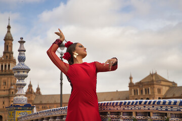 Young teenage woman in red dance suit with red carnations in her hair doing flamenco dance poses....