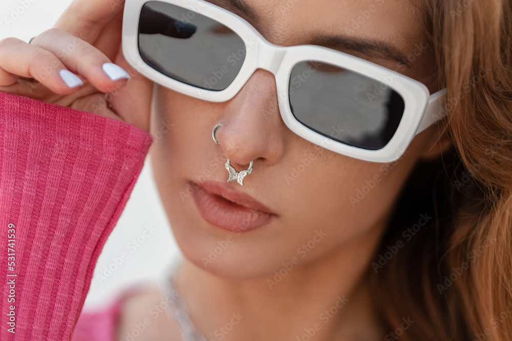 Wall mural Close-up fresh headshot portrait of a beautiful stylish Caucasian redhead girl hipster with a nose piercing wearing fashion white sunglasses outdoors