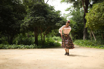 Young teenage woman in pink shirt, black skirt with flowers and pink carnations in her hair, dancing flamenco in an outdoor park. Flamenco concept, dance, art, typical Spanish dance.