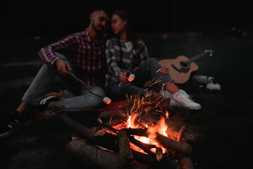 Young loving couple of man and beautiful woman are roasting at fire marshmallows on sticks