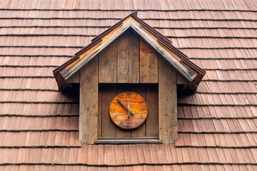 historic dormer with a wooden clock on a shingled roof
