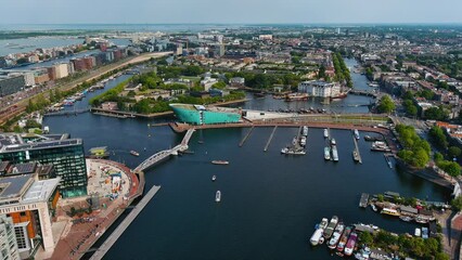 Amsterdam cityscape and NEMO Science Museum with canal boats and aerial skyline in Netherlands. Drone footage of neighborhood in the centrum borough on a beautiful summer day in Holland, Europe 4K