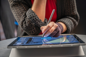 main avec un demi-gant en train de dessiner sur une tablette graphique avec un stylet