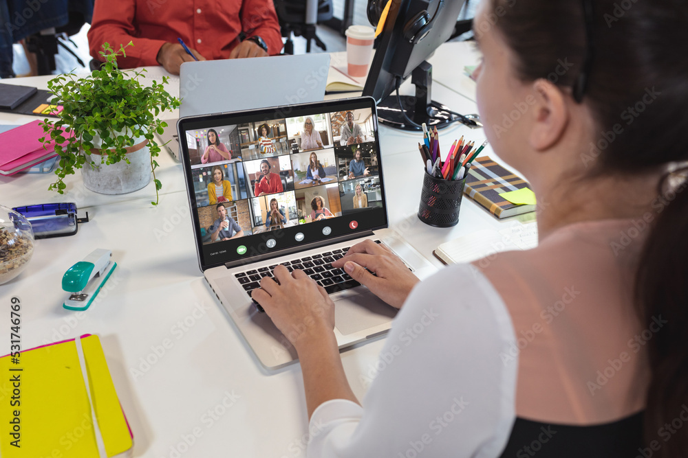 Wall mural Rear view of caucasian woman video conferencing with coworkers over laptop at office