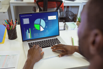 African american businessman analyzing business report over laptop on desk in office