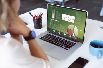 Caucasian businesswoman analyzing business report over laptop on table at office