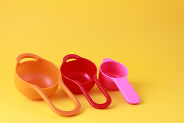 Colorful plastic measuring spoons and measuring cups on bright background with space for text