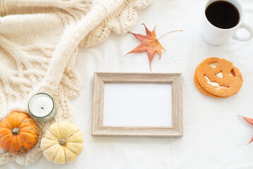 Blank wooden frame mockup whit coffee and cookie. Autumn, fall, halloween concept. Pumpkins and candle on white woolen plaid with decorations