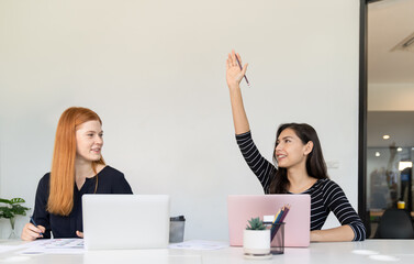 Businesswoman raising her hand and asking questions while meeting with colleague in office.Young woman use laptop and share idea with business team.