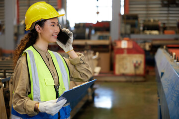 female factory workers or engineer talking on smartphone and holding a clipboard in the factory