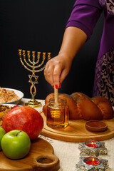 Honey drips from a wooden spoon in a woman's hand next to the menorah challah and couscous and pomegranate.