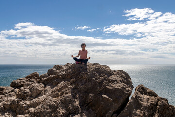 Obraz premium Woman doing yoga on a rock above the sea