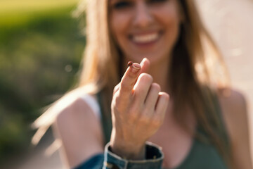 Smiling beautiful woman holding a ladybug while showing it to camera in rapessed field. © nenetus
