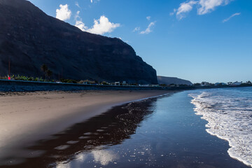 Scenic view on beach Playa Valle Gran Rey at early morning seen from Promenade La Calera in Valle Gran Rey on La Gomera, Canary Islands, Spain, Europe. Mountain reflections in dark volcanic sand beach