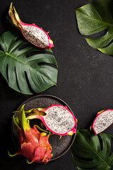 Tropical pitaya fruit on a black plate and green leaves on the black background. Vertical background splash with tropical fruits 
