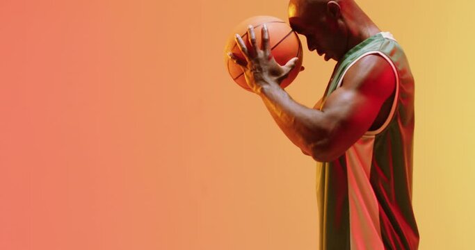 Video of african american male basketball player holding ball on orange background