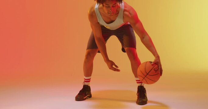 Video of biracial male basketball player bouncing ball on orange to yellow background