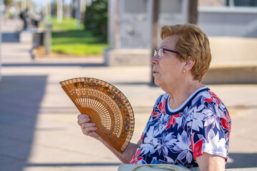 Close portrait, older woman with a hand fan outdoors