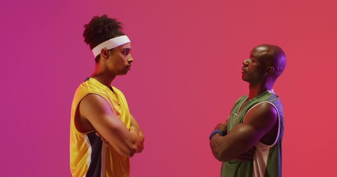 Video of two diverse male basketball players facing each other on pink background
