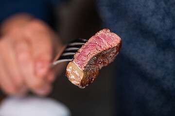 Man is holding a piece of medium rare steak on a fork