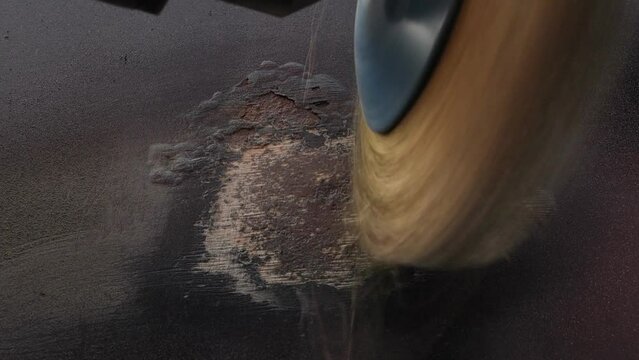 A round metal brush in the hands of a worker polishes paint on a car door. Medium plan