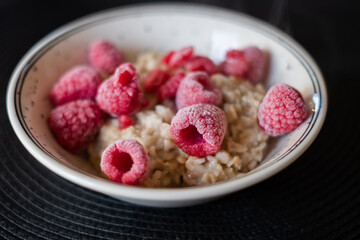 Hot oatmeal porridge with cold frozen berries steaming. Healthy vegetarian breakfast bowl with frozen raspberries. Kids menu.