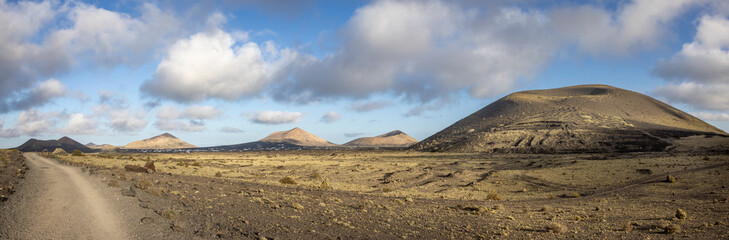 Obraz na płótnie Canvas Panoramic image of the landscape near Montaña Colorada (to the right Montaña Negra) on Lanzarote island, Spain