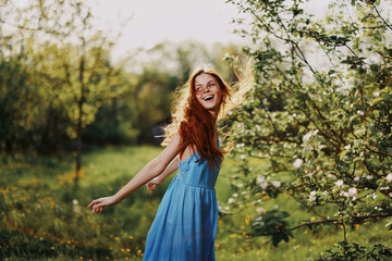 Woman with a beautiful smile with teeth and long hair flying hair spring dance hands up in the sunset in the park near the flowering trees happiness, natural beauty and hair health