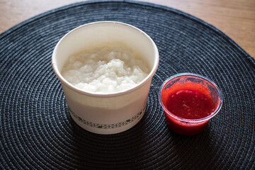 HeRice flake porridge in a white round carton take-away box with fresh strawberry jam. Healthy breakfast bowl delivery food to-go.