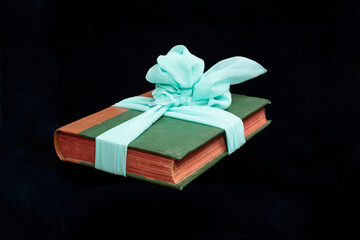 Levitating green book with red pages, tied with a turquoise bow