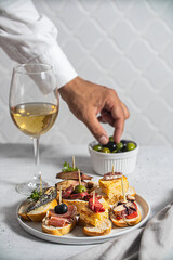 Set of Spanish pinchos with seafood and fish on bread. Man holds an olive