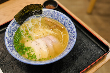 Ramen or Japanese noodles topped with Chashu or boiling pork and scallions in clear soup served in a bowl on brown wooden table