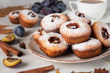 Homemade muffins with plums and cinnamon, sprinkled powdered sugar on round plate on gray background