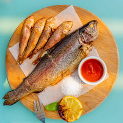 Large and small fried fish on a wooden board, Sauce, salt. close-up.