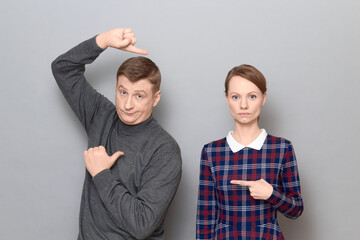 Man and woman pointing at each other, with different face expressions