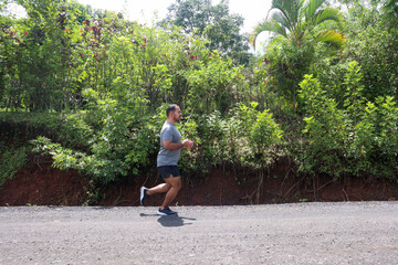 Young mid weight man jogging on the unpaved road with green background