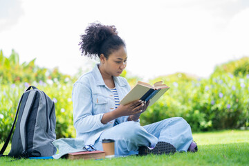 An African woman reading a book in the park. Educational concept. Happy students sit and read books in a green park. Prepare for university. girl reading a book resting in the park relaxing