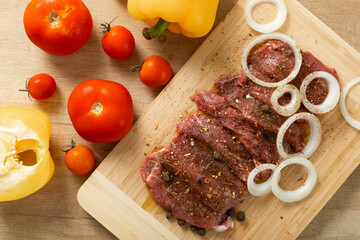 Raw beef with onions marinated with spices on light texture background.Meat cooking recipe.Juicy steak on a bamboo board, close-up. Place for text, space for copy.