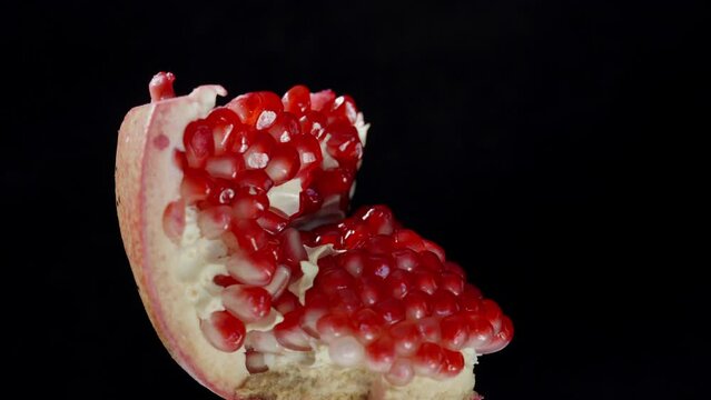 The pomegranate fruit, broken in half, rotates on a black background, close-up