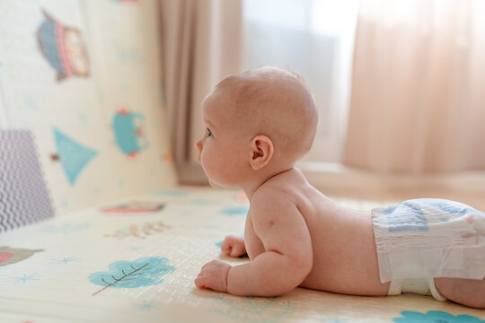 A cute chubby baby lies undressed on the carpet and happily looks at the pictures