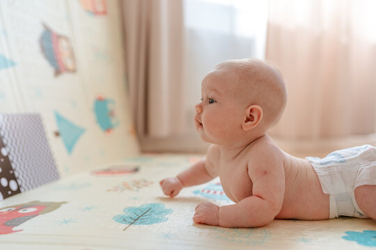 A cute chubby baby lies undressed on the carpet and happily looks at the pictures