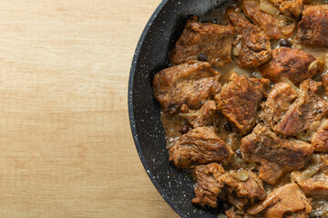 Fried beef with onions and spices in a frying pan on a light texture background. Meat recipe. Juicy grilled steak, close-up. Place for text, space for copy.