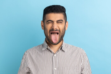 Photo of young handsome foolish crazy businessman, keeping eyes closed and showing tongue out,...