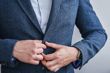 Business man fastens a button on blue tweed blazer, hands close-up.