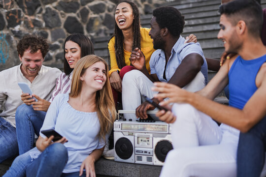 Group of young diverse millennial friends having fun together in the city while listeing music with old vintage boombox