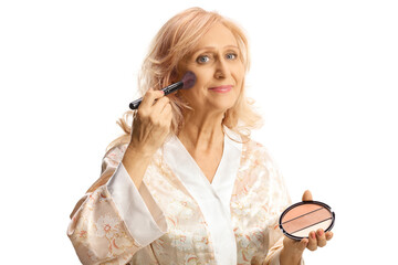 Mature woman in a silk bathrobe applying blush on cheek with a brush