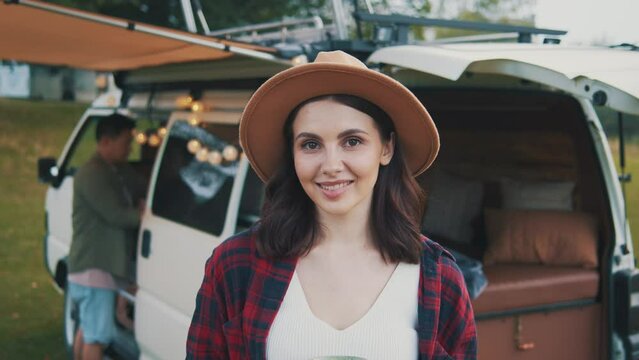 Portrait of young woman with hat standing looking on camera smiling on travel trip. On background rv car. Motorhome travel trip. Vacation. House on wheels